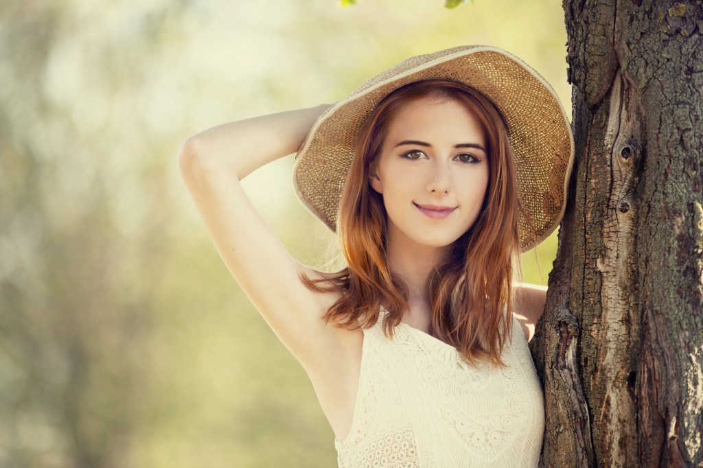 Redhead girl with hat near tree.